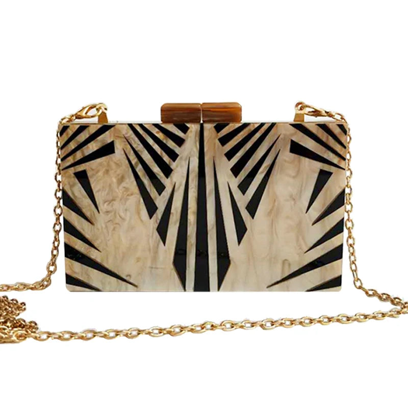 Front view of the Deco Lux Clutch, featuring a black and ivory sunburst pattern, with a detachable gold-tone chain.